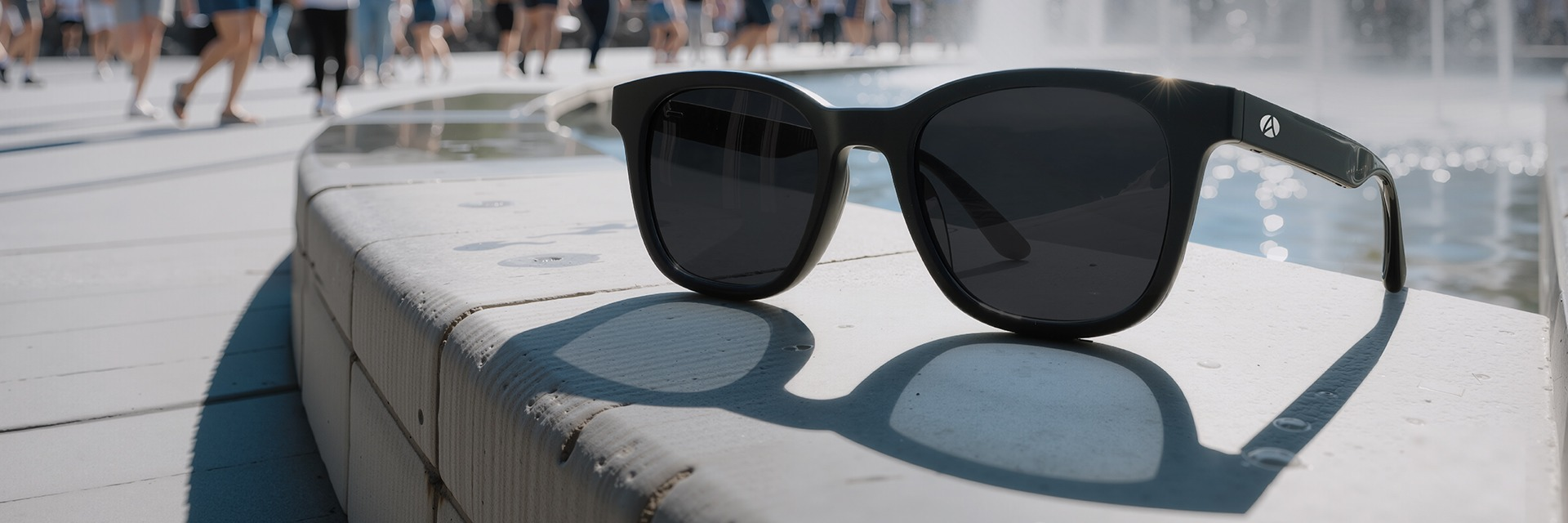 A pair of electrochromic sunglasses changing the level of dark vs transparent as the pages scroll, laying on a concrete ledge in front of a fountain.